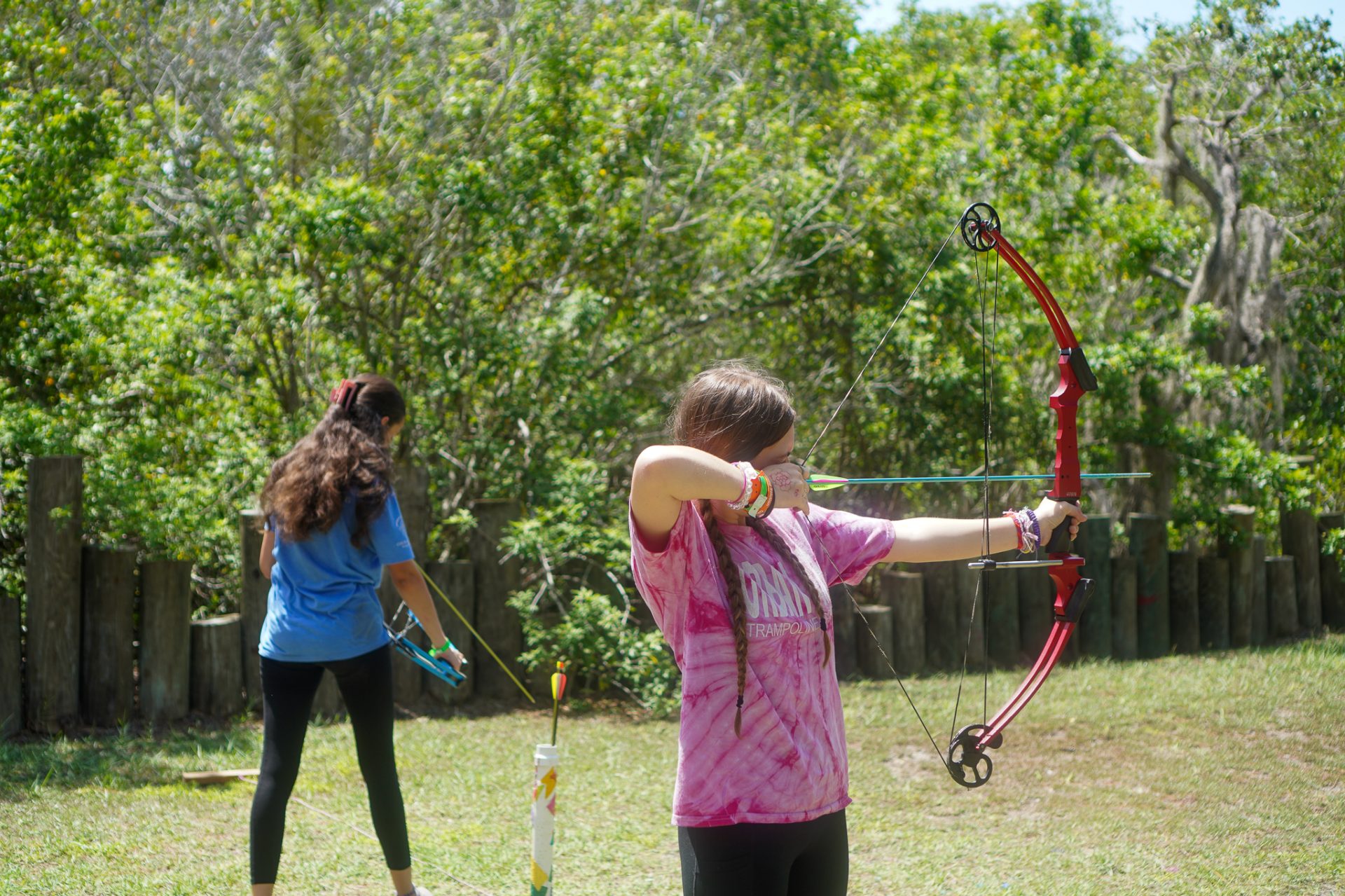  A preteen girl in a pink shirt holding a bow and arrow at Camp Wai Lani. 