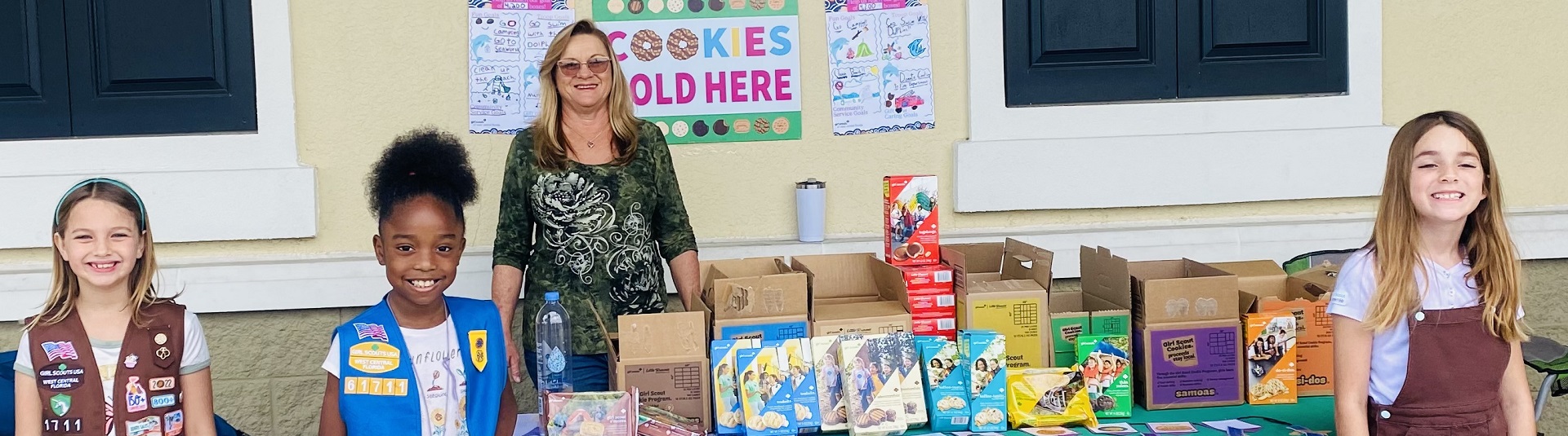  hands of young girl scout holding cookie box and handing it to a customer at an outdoor cookie booth 