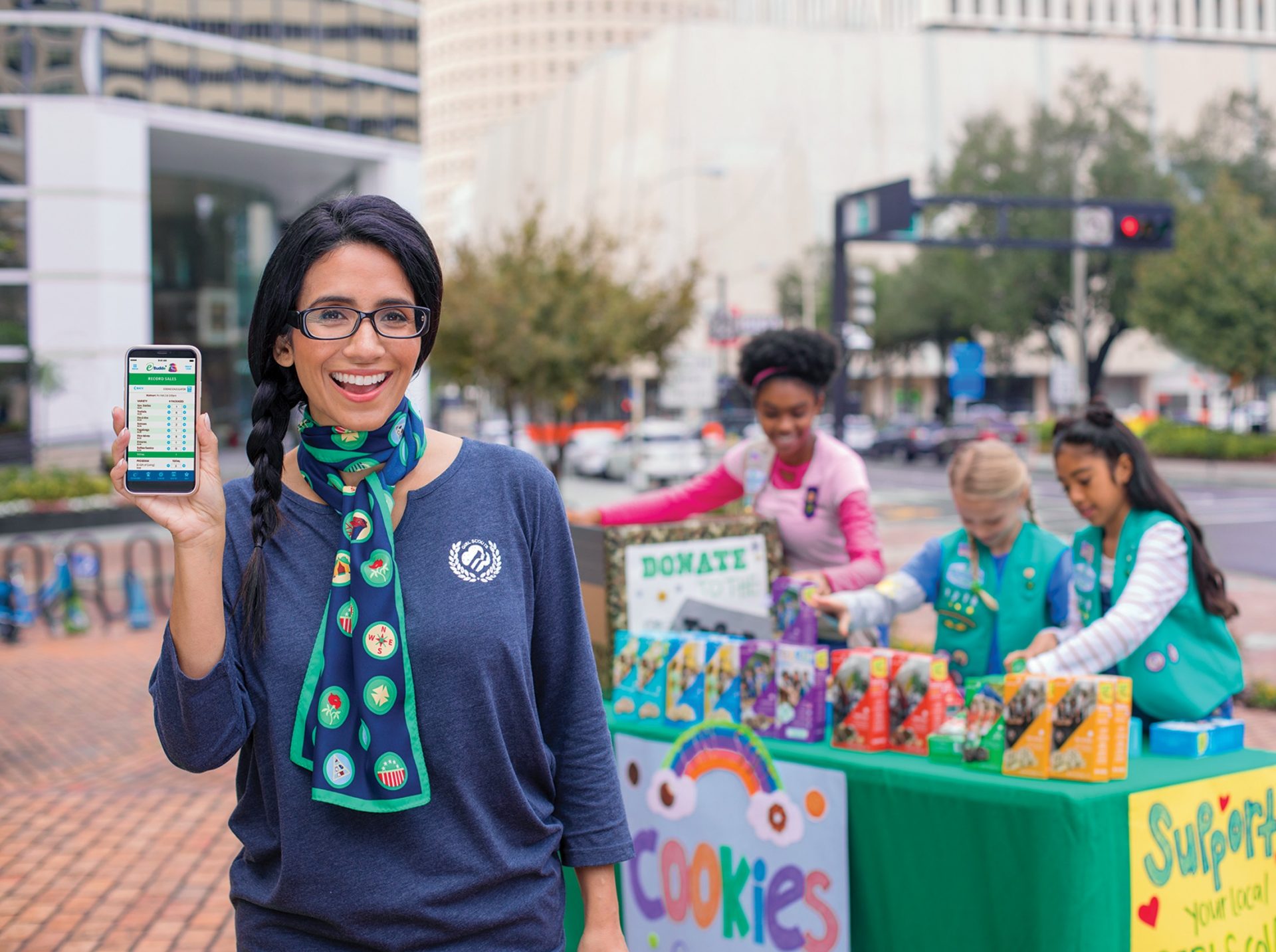 volunteer with junior girl scouts at outside cookie booth smiling