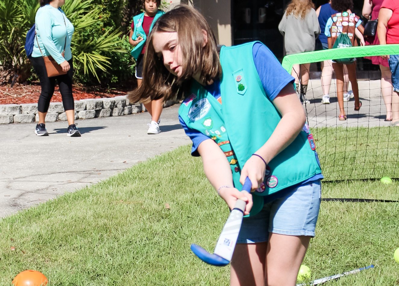 young girl scout gardening with orange watering can outdoors at park